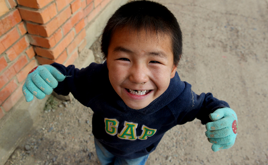 A little boy in Mongolia smiles up at the camera.